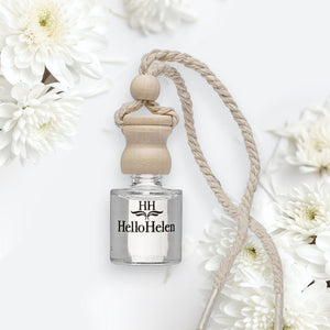 Diffuseur de voiture HelloHelen : petit flacon en verre à bouchon de bois et cordelette, parmi des fleurs blanches